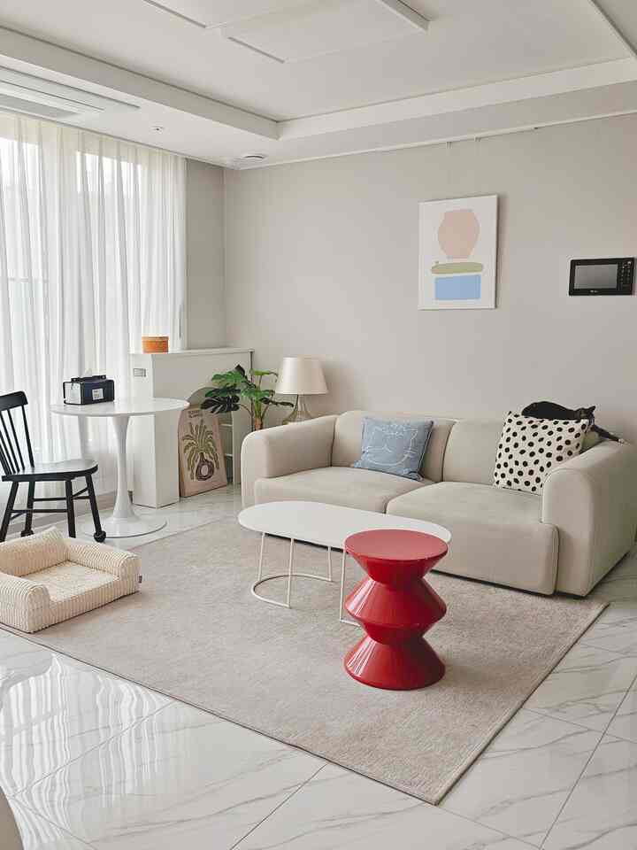 Beige and white toned living room featuring a beige sofa, white coffee table, pet sofa, and a cat, creating a natural modern atmosphere