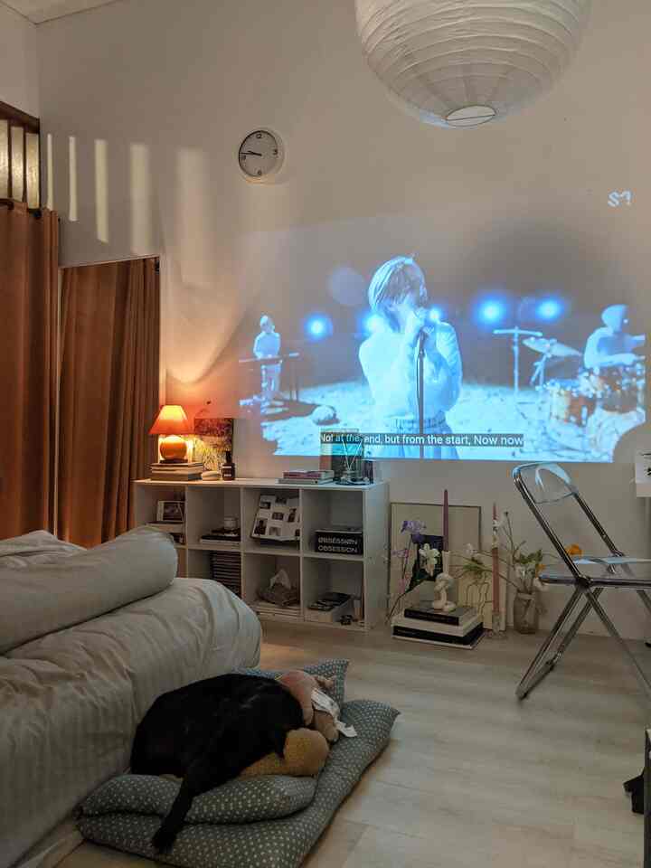 Soft white and brown toned bedroom featuring a low bed and projector screen creating a cozy nighttime atmosphere