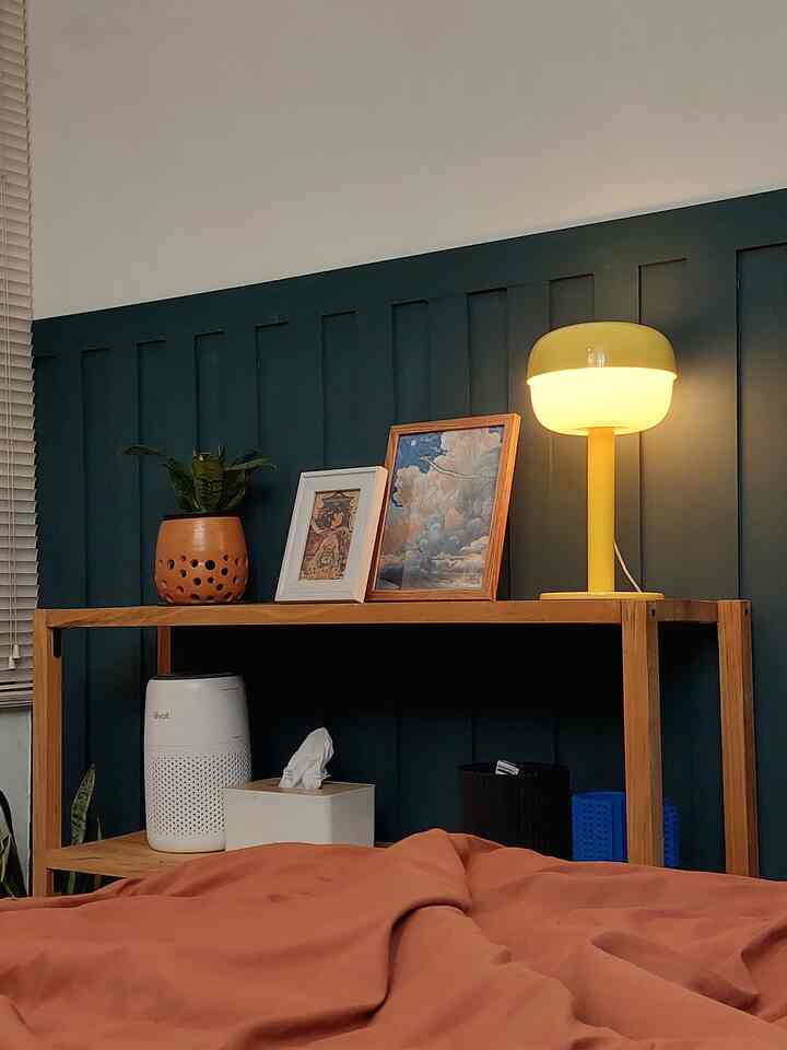 Natural brown-toned bedroom with wooden shelf displaying picture frames and a yellow table lamp, creating a cozy atmosphere