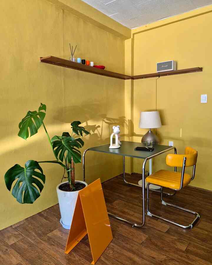 明るい黄色の壁と木目調の床が調和したダイニングルーム、黄色のクッションチェアとダイニングテーブル、大きなモンステラの植物が配置されたモダンな空間