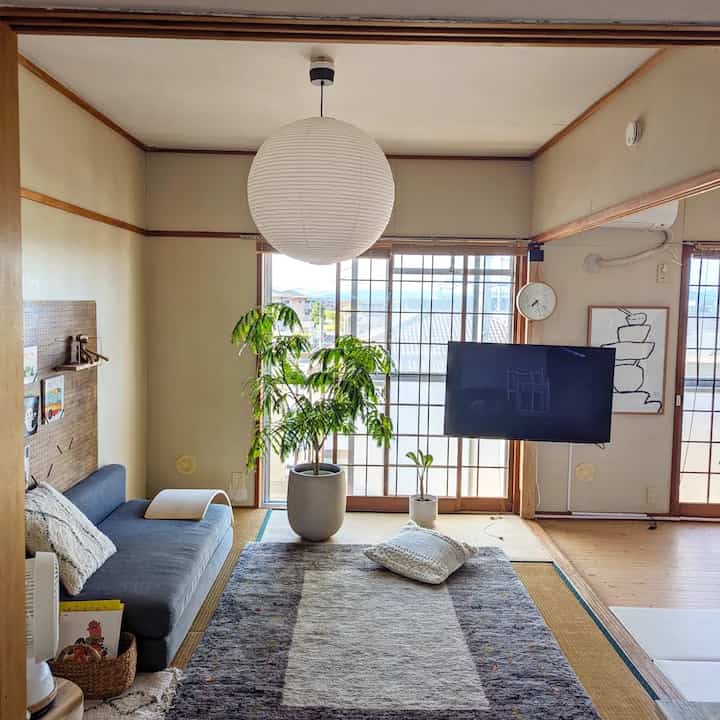 白を基調とした和風リビング、大きな観葉植物とダークグレーのソファが配置された自然で伝統的なインテリア