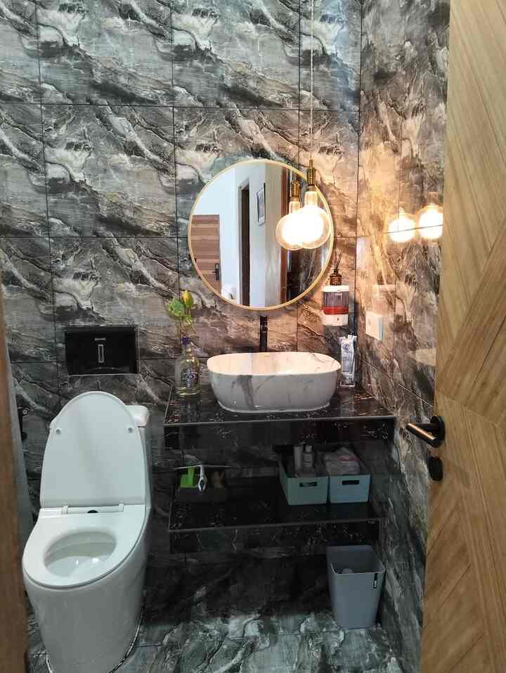Black-toned compact bathroom featuring round mirror and pendant light in a hotel-like style