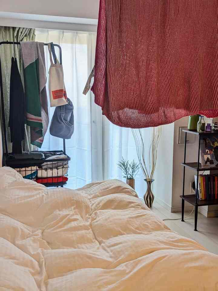 ベージュの寝具を中心とした明るい寝室、ピンクのブランケットが掛かり、ナチュラルな植物が調和した雰囲気のあるインテリア