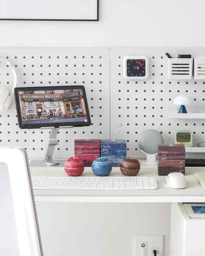 白とグレーのトーンのホームオフィスデスク、丸いキャンドル3つとタブレットスタンドが置かれたシンプルな作業空間
