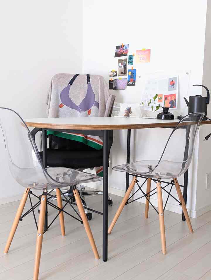 明るいホワイトトーンの壁と床、透明なダイニングチェアと木製の脚があるモダンなダイニングスペース