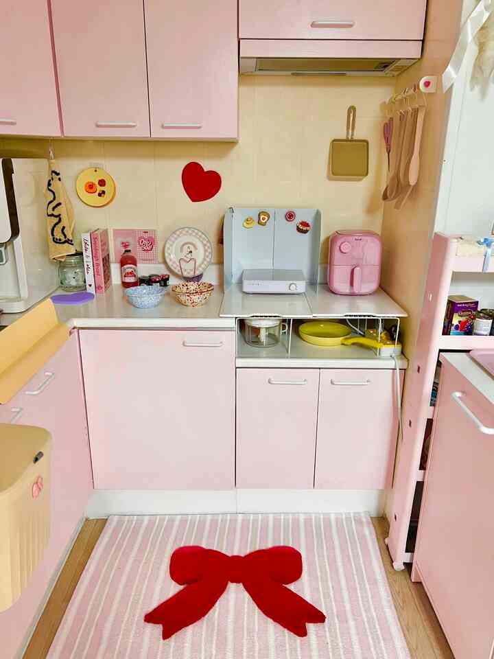パステルピンクのキッチン、ピンクのキャビネットと調理器具が配置されたかわいらしい雰囲気のあるインテリア