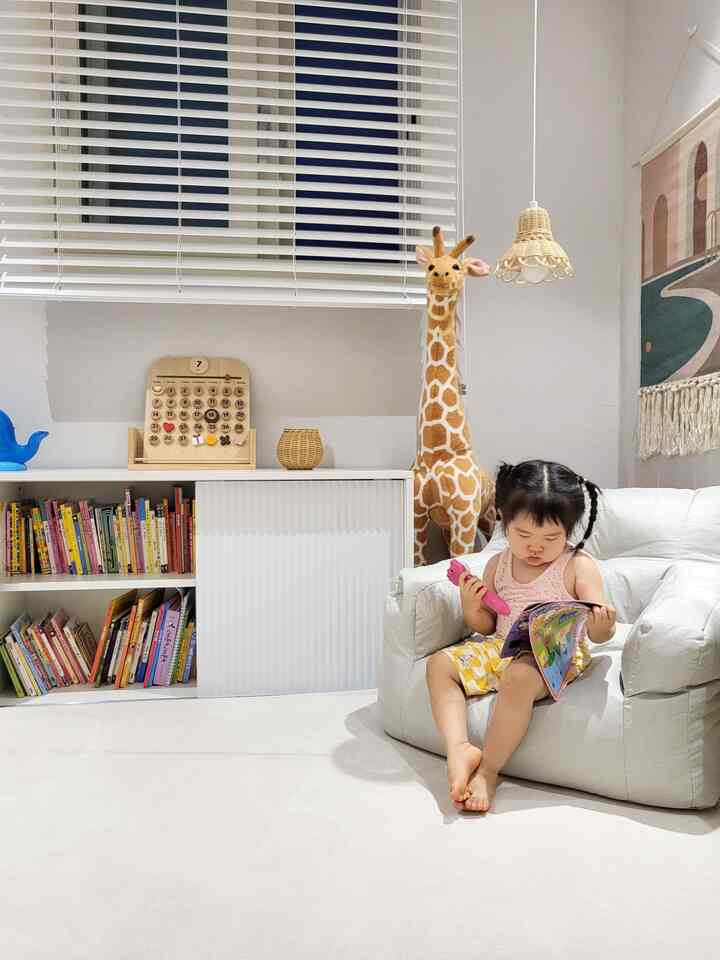 ホワイトとウッドトーンが調和した子供部屋、ビーズクッションソファに座って本を読む子供がいる雰囲気のある空間