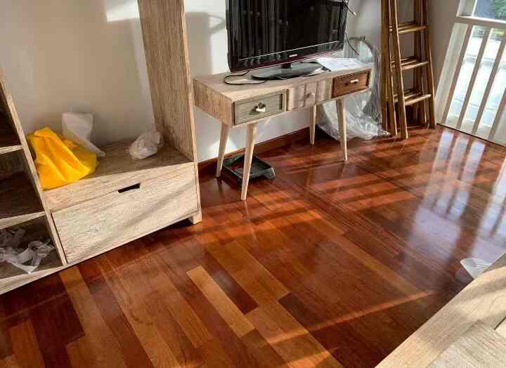 Warm wood tone flooring with natural furniture in a compact living room space, bright atmosphere with sunlight streaming in