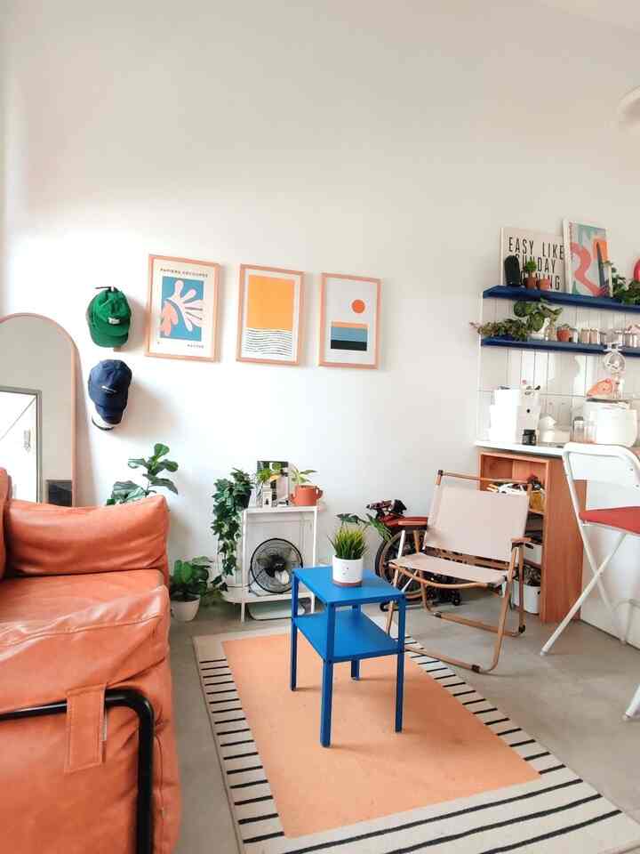 Orange and blue toned studio living room featuring a leather sofa, side table, and various plants creating a cozy home cafe atmosphere