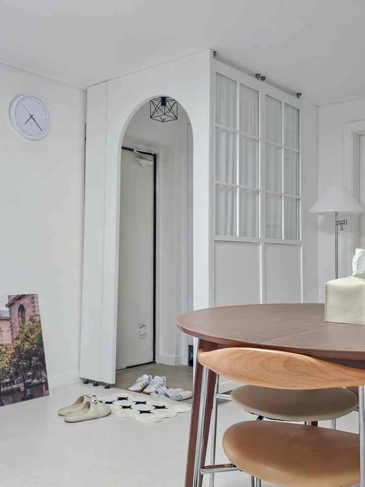 ホワイトと木目調のダイニングルーム、間仕切りとしてのホワイトパーティションと丸テーブルが配置された清潔感と温かみのある空間