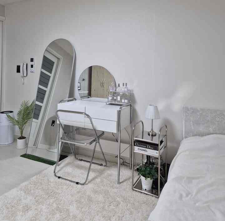 白とシルバーのトーンが特徴のワンルーム、化粧台と全身鏡、シンプルな家具が配置されたミニマルな雰囲気のインテリア