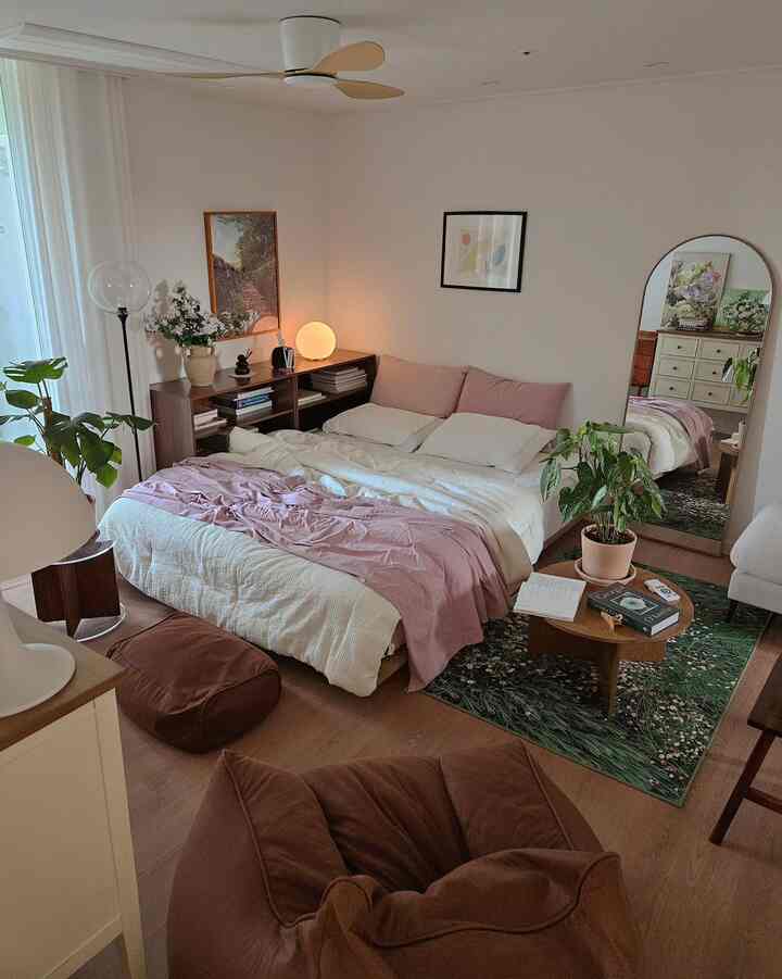 ライトブラウンの木目調とピンクの寝具が調和するくつろげる二人用寝室、植物と照明が配置されたナチュラルモダンなインテリア