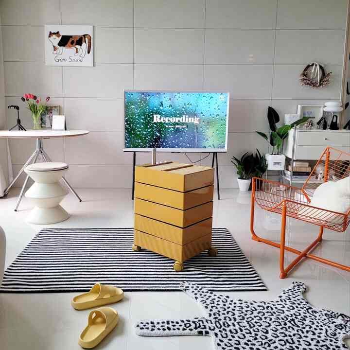 Bright white tiled living room with yellow drawer unit in mid-century modern style, featuring an orange metal chair and cat illustration, cozy home office setup
