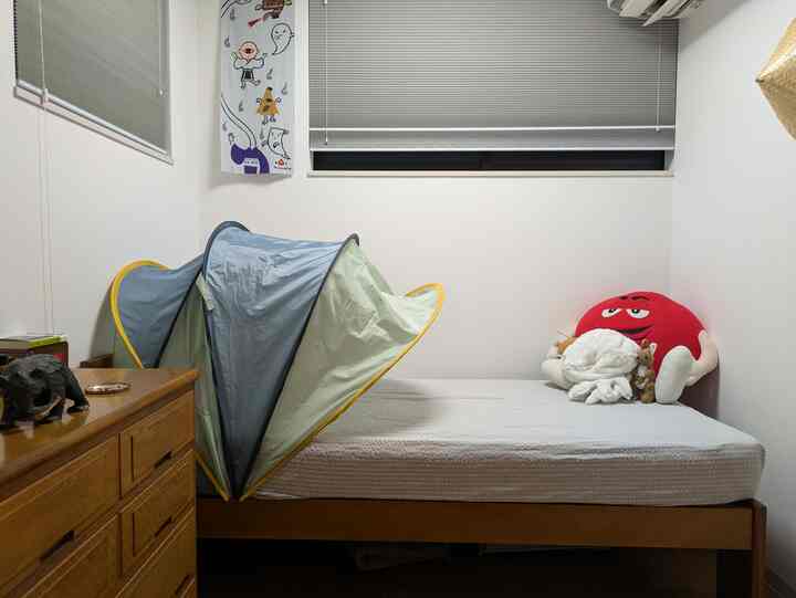 白い壁と木目調の子供用ベッド、チェストが配置された子供部屋。ベッドの上にはぬいぐるみとポップアップテントがあり、温かみのある雰囲気のインテリア。