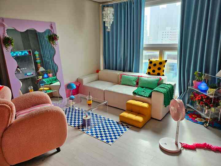 ベージュとブルーの色調のリビング、3人掛けソファとピンクのアームチェア、黄色のペットステップ、青いテーブルランプが調和した雰囲気のあるインテリア