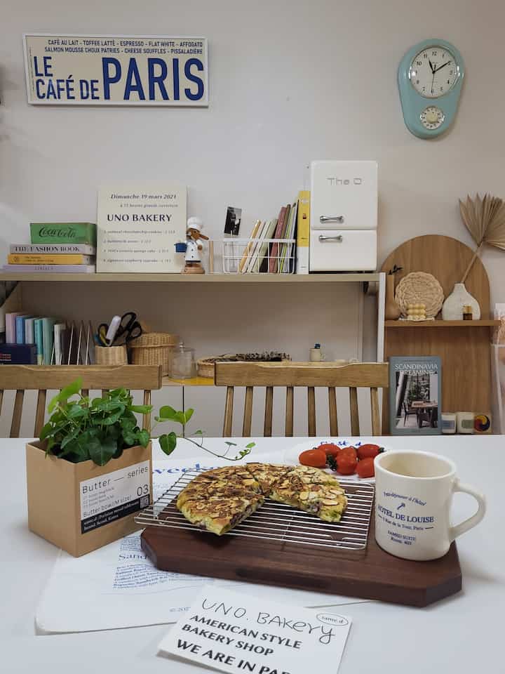 ナチュラルな色調のダイニングルーム、フレンチカフェ風の本棚とホームカフェアイテムが配置された雰囲気のあるインテリア