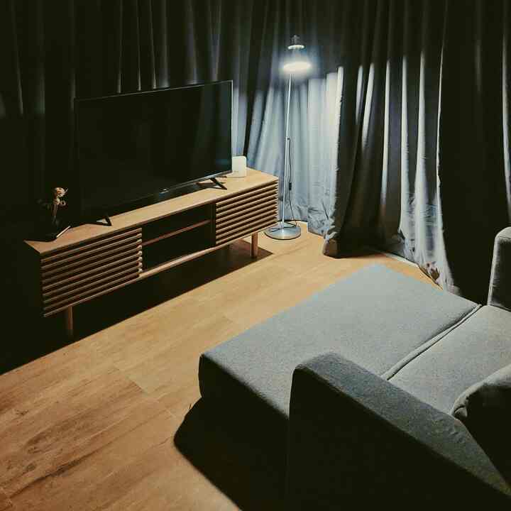 Natural wood tone floor and TV stand in living room, gray sofa bed and floor lamp creating cozy night ambiance