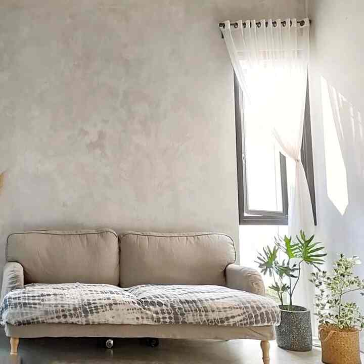 Simple living room with gray tones and natural-colored furniture featuring beige sofa and plants, creating a spacious and airy atmosphere