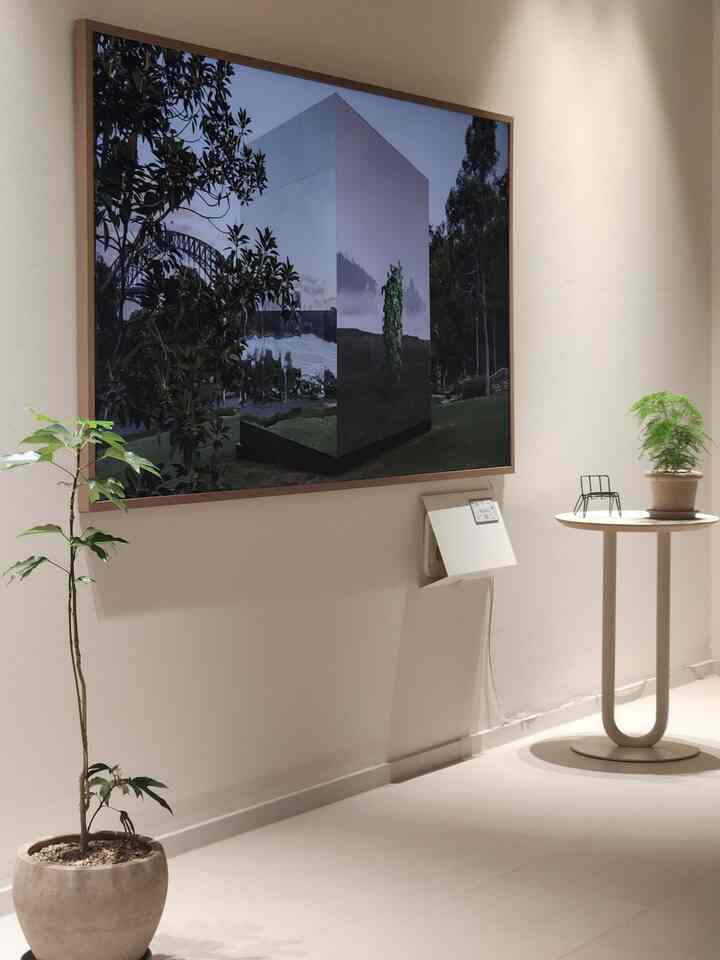 アイボリー調のリビングの壁に大きな額縁が掛けられ、植物とサイドテーブルが配置されたミニマルで自然な雰囲気のあるインテリア