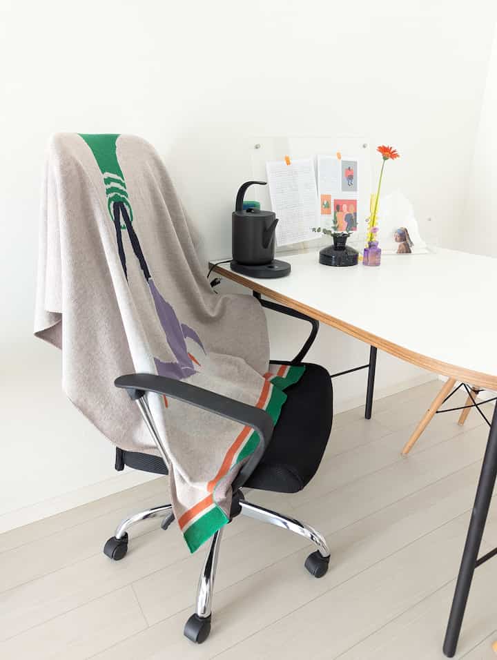 白とナチュラルカラーのホームオフィス、黒のオフィスチェアとダイニングテーブル上の電気ケトルが配された、雰囲気のある作業空間