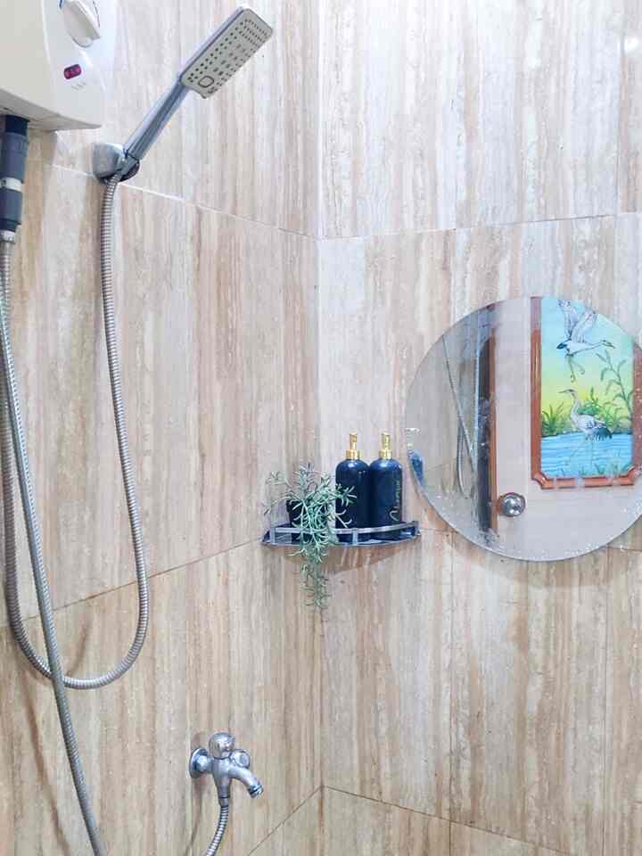 Cream and natural-toned bathroom with corner shelf, round mirror, and hand shower creating a cozy atmosphere