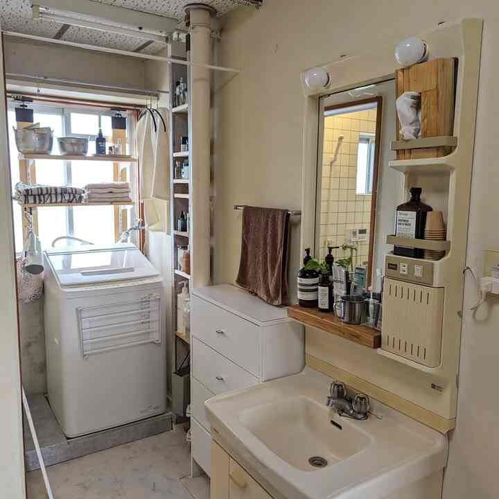 白を基調とした狭く縦長のランドリー兼洗面所、洗濯機や収納がありDIY感のある実用的なインテリア