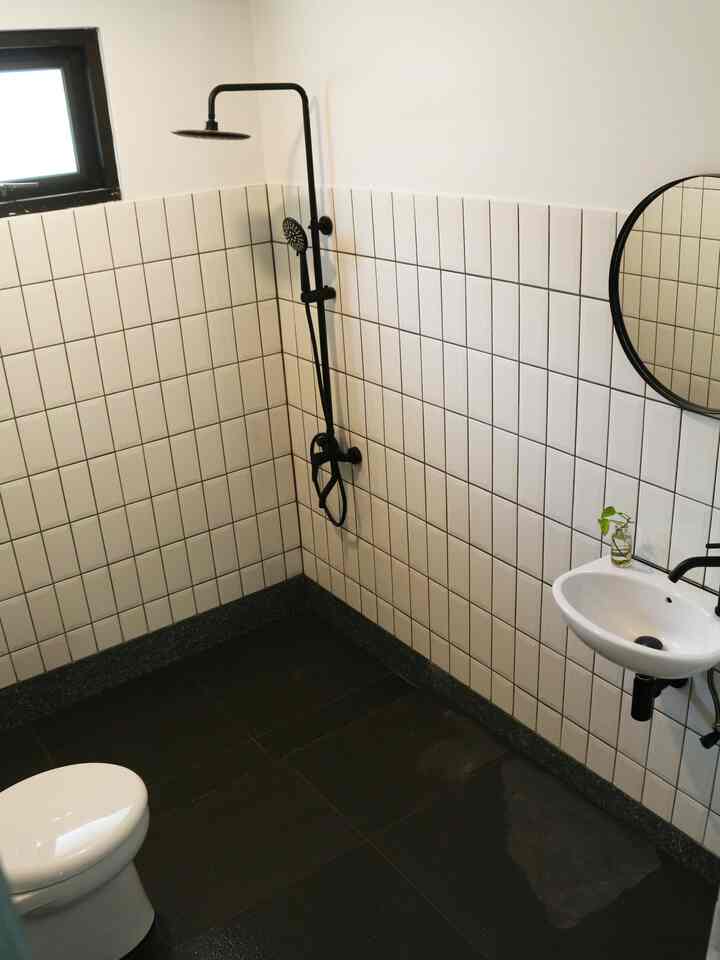 Minimal black and white toned small bathroom featuring sink, shower, and toilet with clean modern design