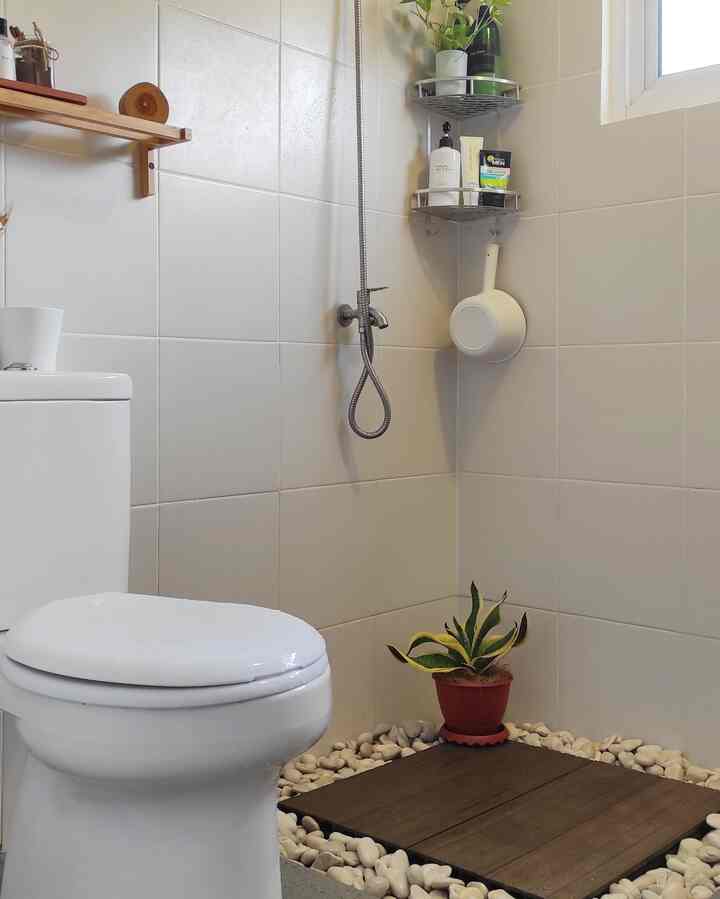 Bright narrow bathroom with white walls and wood-tone flooring, featuring toilet and shower area in a clean, tidy space