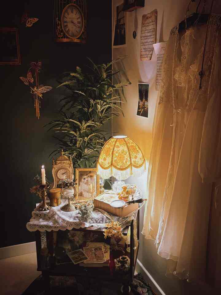 温かみのあるベージュとブラウン調の寝室の一角、ヴィンテージのナイトテーブルとレトロな壁時計、キャンドルと花瓶が調和した雰囲気のあるインテリア