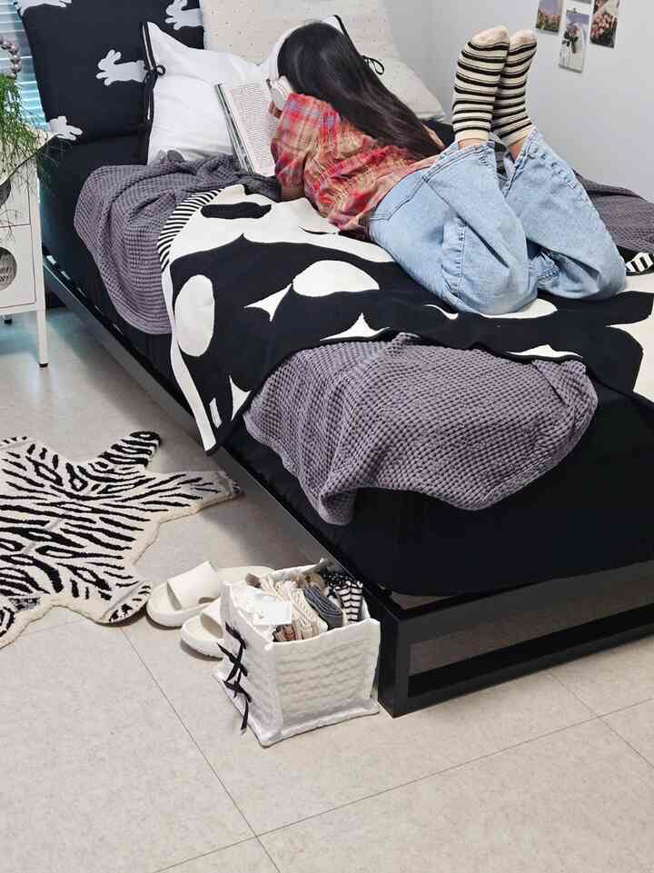 ブラックとグレーのトーンの寝室、中央に黒いベッドとグレーのブランケットが配置され、一人の人がベッドで読書している印象的な空間