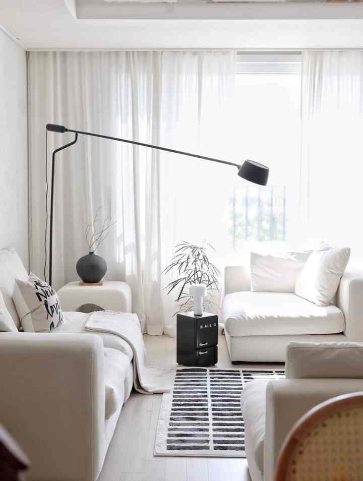 Bright white-toned living room featuring modular white sofas, a black floor lamp, and a patterned rug with a simple, natural interior style