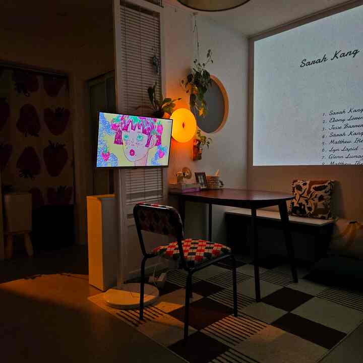 Small modern dining room with warm orange wall sconce, red plaid chair, and wall-mounted TV creating cozy atmosphere
