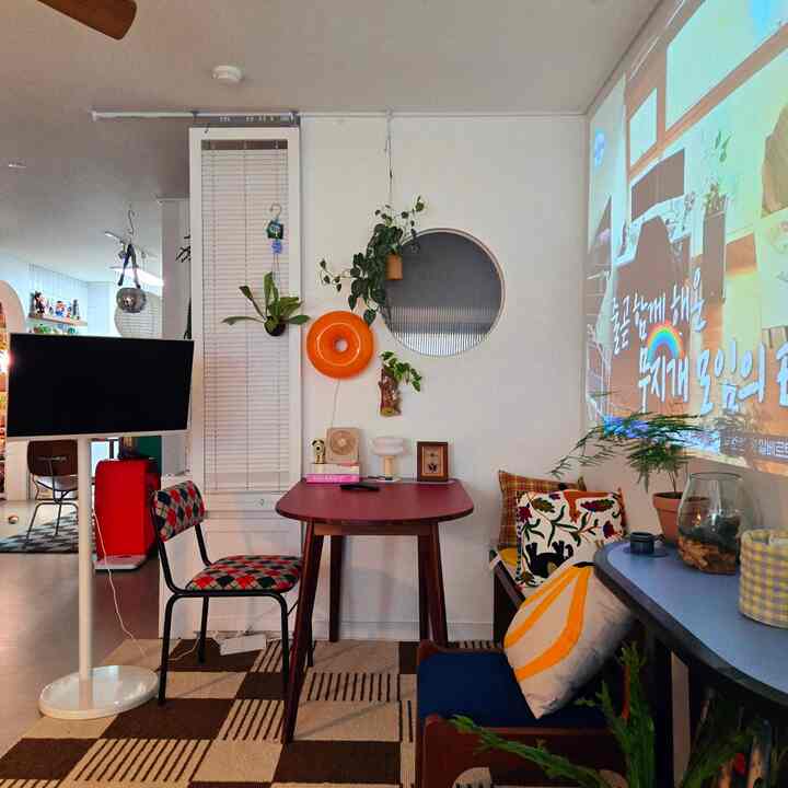 Dining room with white walls and wood tone furniture, featuring a projector screen, plants, and cushions creating a cozy atmosphere