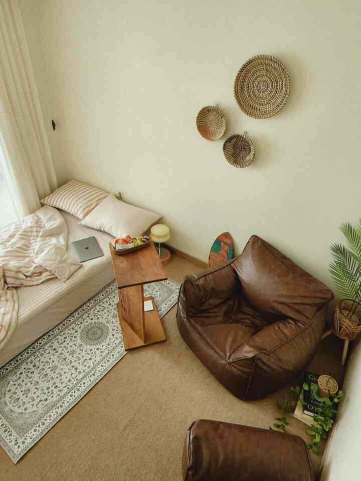 ナチュラルカラーのワンルーム、ブラウンのアームチェアとベッド、ラグが配置された落ち着いた雰囲気のインテリア