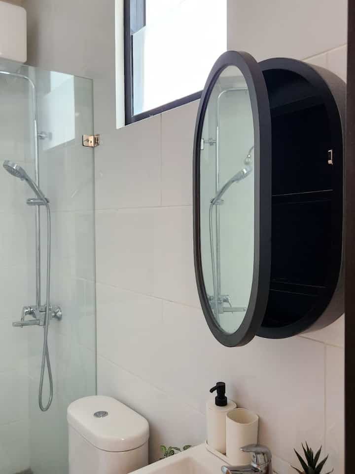 White-tiled bathroom featuring a black oval cabinet mirror, shower fixtures, and toilet, creating a clean and minimal look