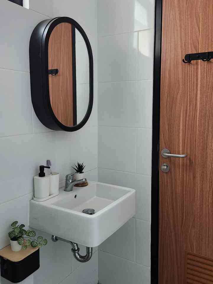 Bright white and wood-toned narrow bathroom space featuring a wash basin, oval mirror, and small plants with a clean atmosphere