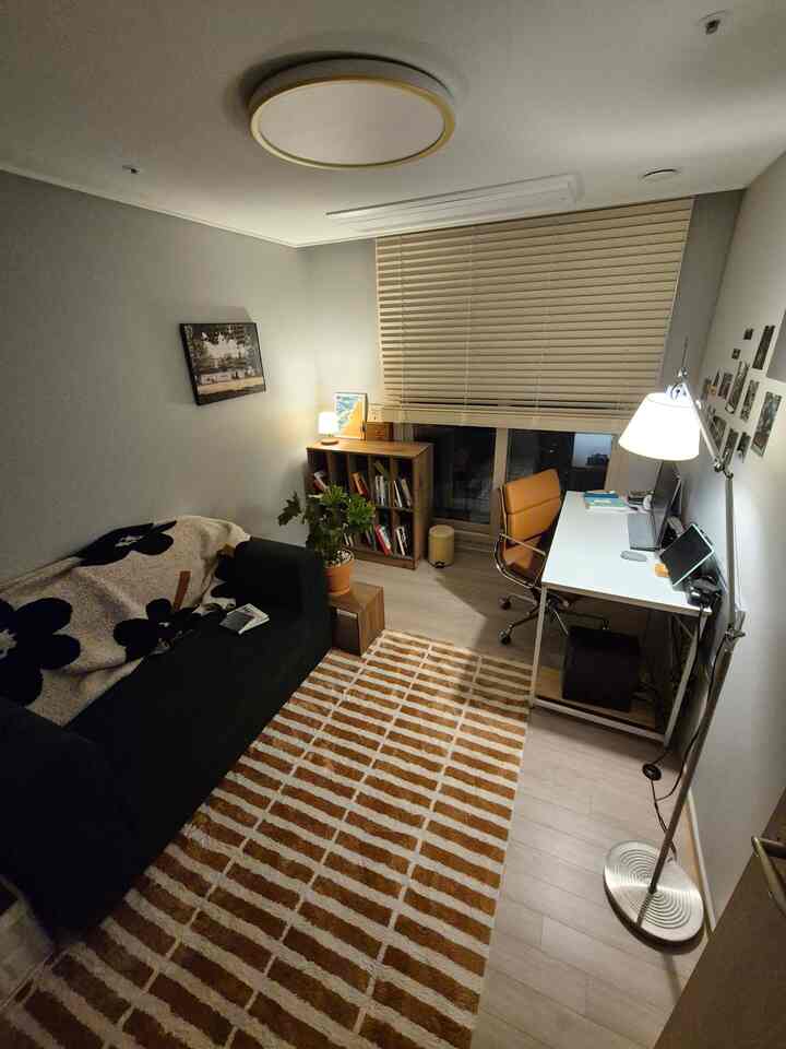 ブラウンの木目調と白を基調としたモダンな書斎、ダークグリーンのソファとストライプのラグが配置された落ち着いた空間