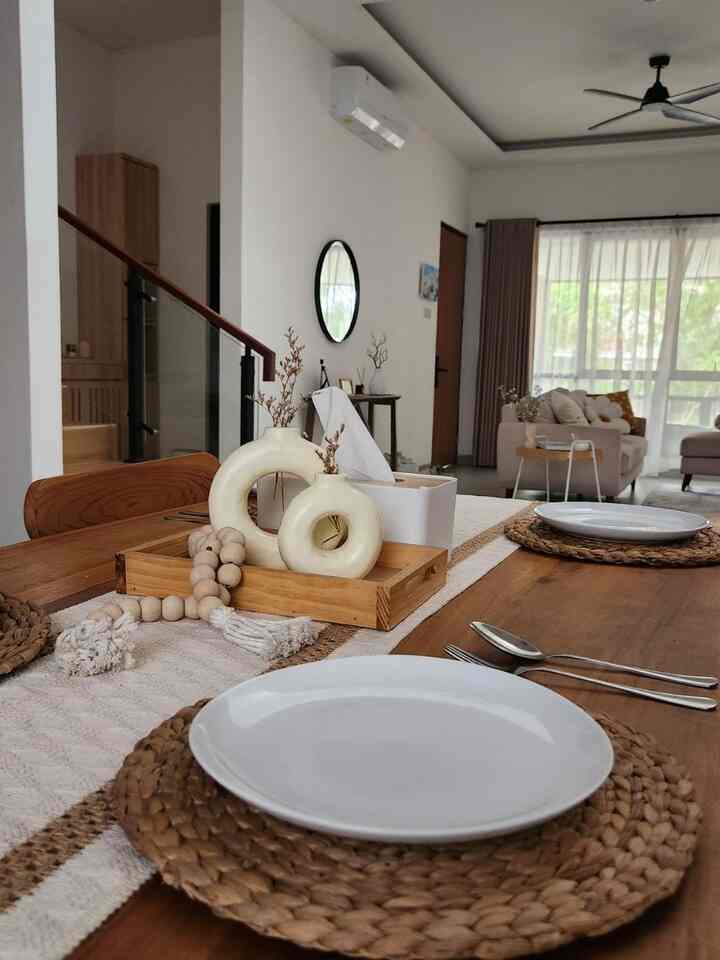 Natural dining room with white walls and wood tone dining table, accompanied by living room visible in the background
