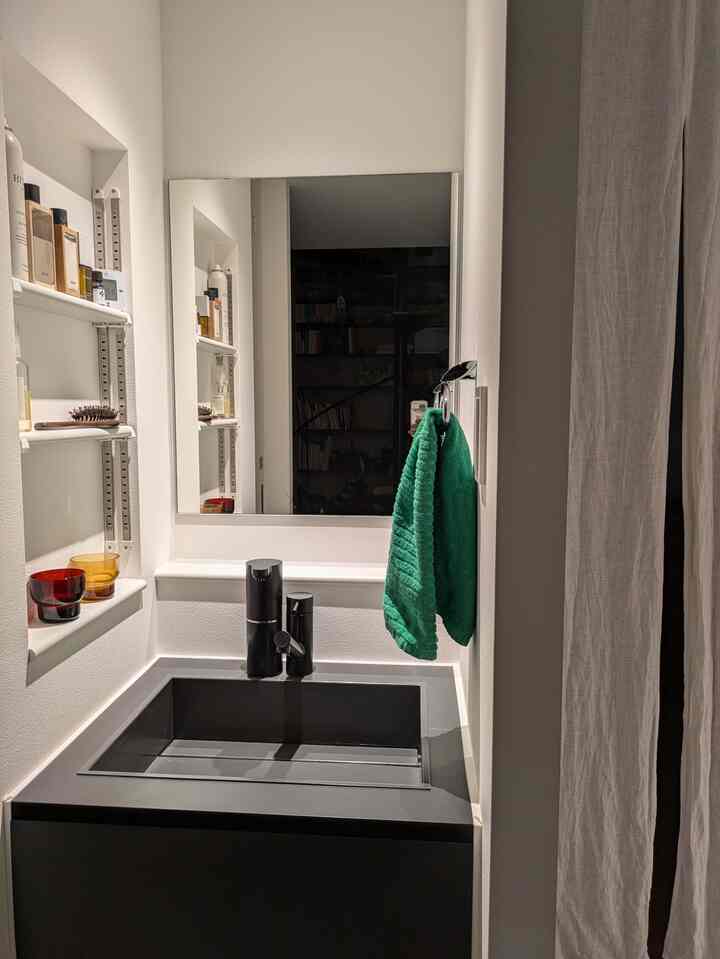 Compact modern bathroom with white walls and shelving, featuring a black sink centered and a green towel hanging on the right