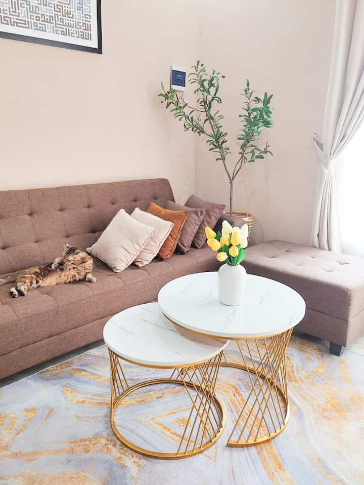 Cozy living room with natural brown sofa and white round coffee tables, featuring a vase with flowers and a green plant
