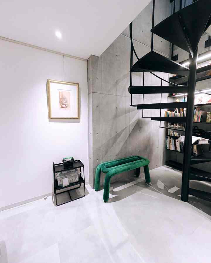 グレーとホワイトの色調の狭い部屋、黒い螺旋階段と緑のベンチが配置されたモダンな空間