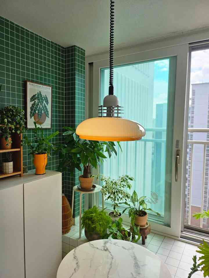 Cozy home cafe space with deep green tiled wall, white marble table, and multiple plants arranged