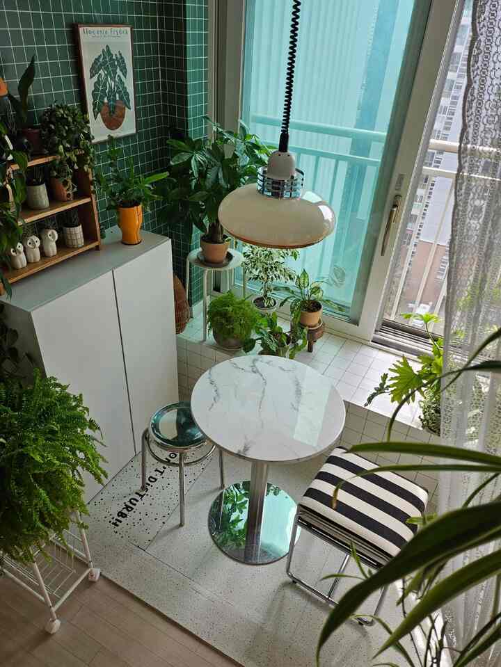 Cozy home cafe space with green tiled walls, white marble round table, striped stool, and abundant plants
