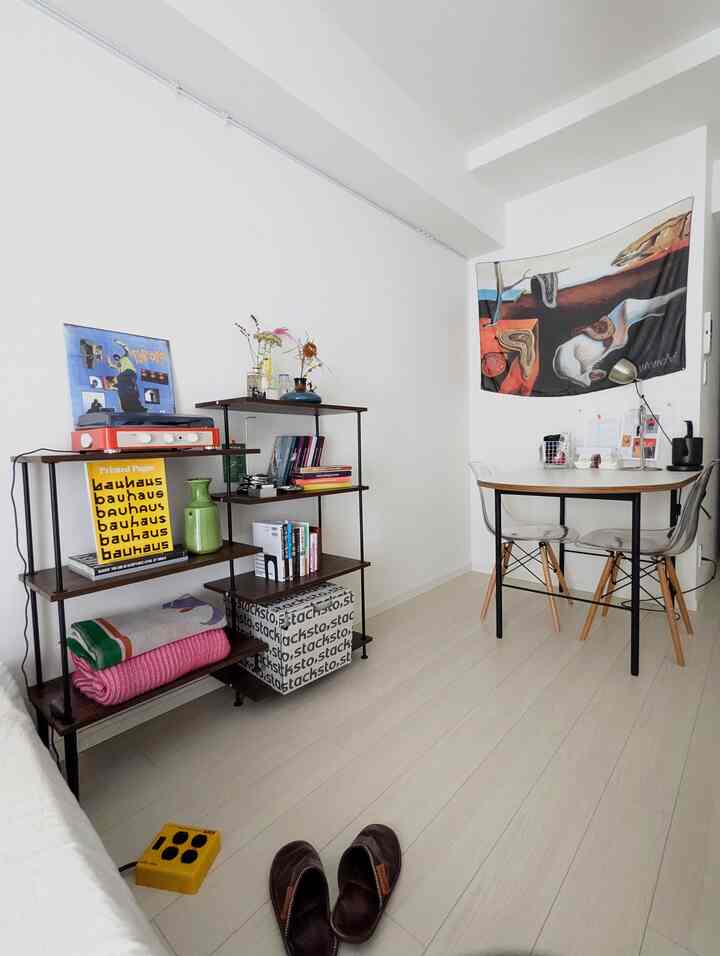 Modern dining room with white floors and walls, transparent chairs, and dark wood rack shelving