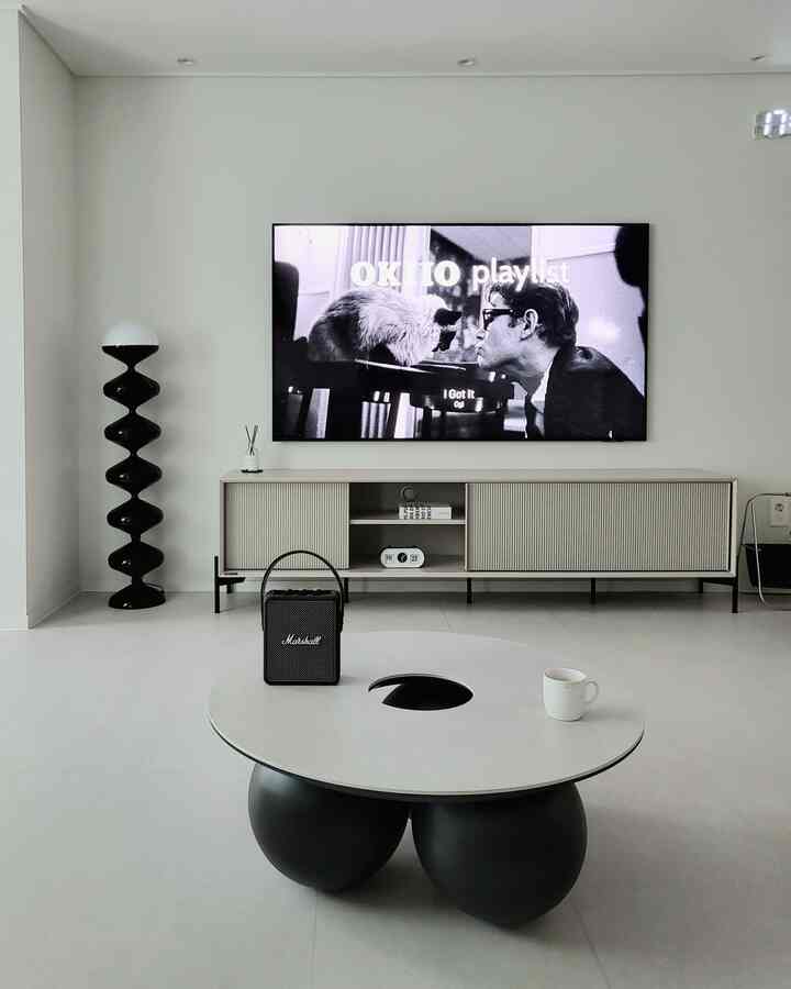 モノトーンでミニマルなリビング、特徴的な丸いコーヒーテーブルとテレビスタンド、フロアランプが配置された雰囲気のある空間
