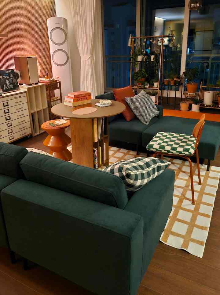 ダークグリーンのソファと木製のコーヒーテーブル、多様な植物が配置された暖かみのあるレトロなリビング空間