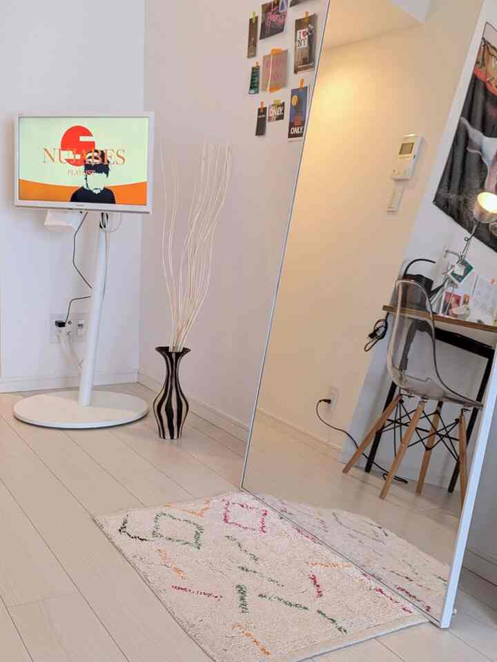 明るいホワイトトーンのワンルーム、印象的な全身鏡とシンプルなデスク、テレビ台が配置されたモダンで清潔感のあるホームオフィス空間