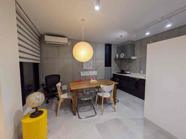 A modern kitchen with gray concrete walls featuring a natural wood dining table and chairs.