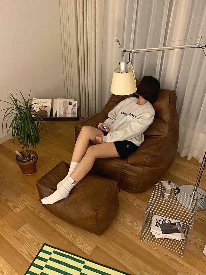 暖かいブラウンとウッドトーンのリビング、ゆったりしたビーズクッションとスツールがくつろぎの空間を演出するインテリア