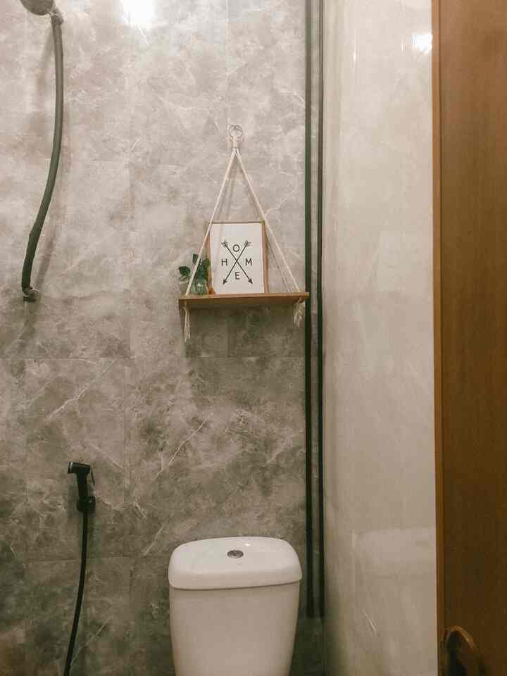 Gray and brown toned compact restroom featuring a white toilet, wooden shelf, and natural elements in Japandi style